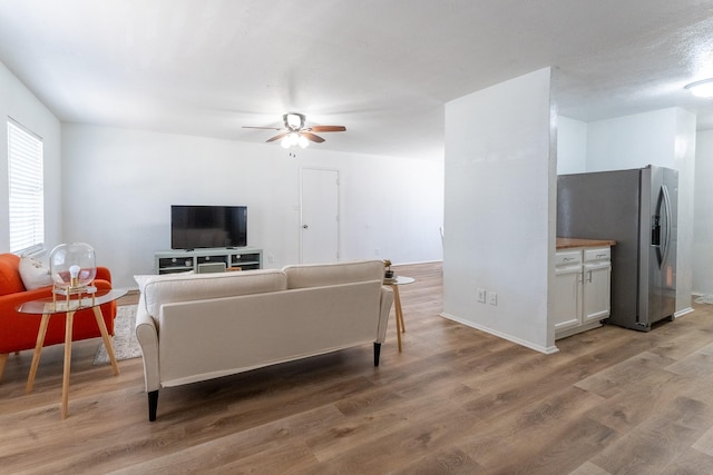 living area with ceiling fan, light wood finished floors, and baseboards