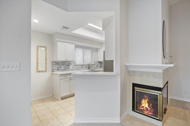 kitchen with a tile fireplace, white cabinetry, sink, backsplash, and light tile patterned floors