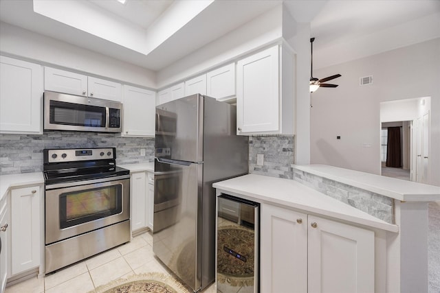 kitchen featuring appliances with stainless steel finishes, white cabinetry, wine cooler, light tile patterned flooring, and kitchen peninsula