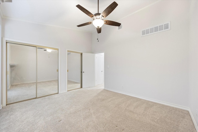 unfurnished bedroom with multiple closets, light colored carpet, ceiling fan, and a towering ceiling