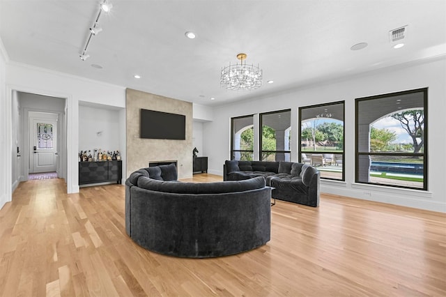 living room with a fireplace, rail lighting, ornamental molding, a notable chandelier, and light wood-type flooring