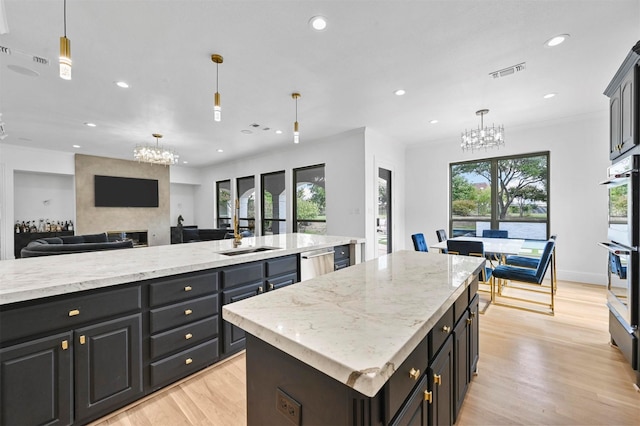 kitchen with stainless steel appliances, decorative light fixtures, sink, and a center island with sink