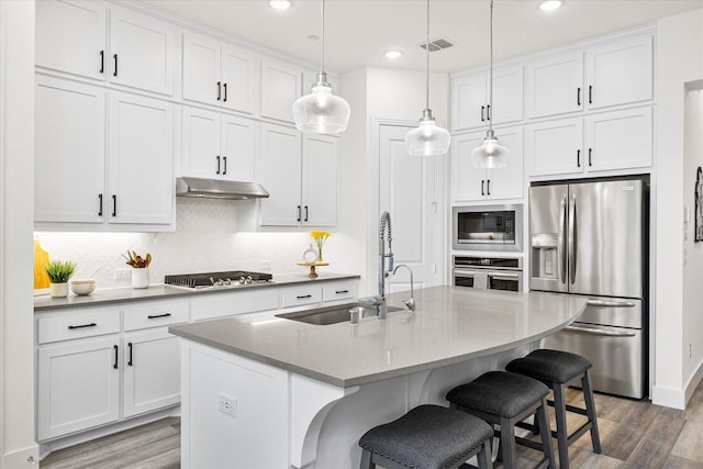 kitchen with a kitchen island with sink, decorative light fixtures, white cabinets, and appliances with stainless steel finishes