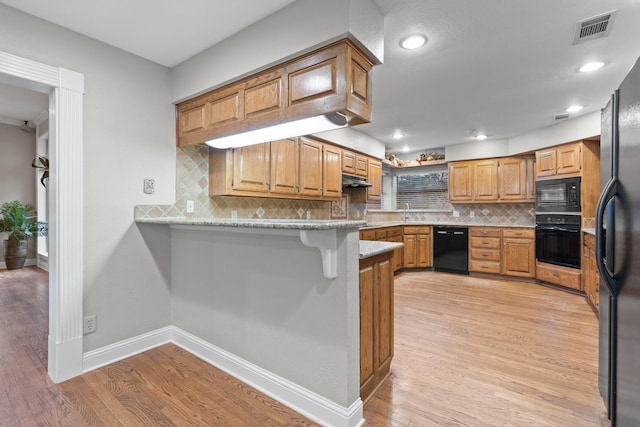 kitchen featuring light hardwood / wood-style floors, black appliances, kitchen peninsula, and a kitchen bar