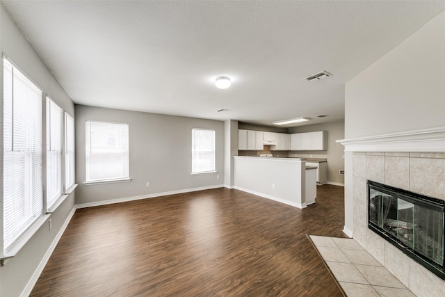 unfurnished living room with a tiled fireplace and dark hardwood / wood-style flooring