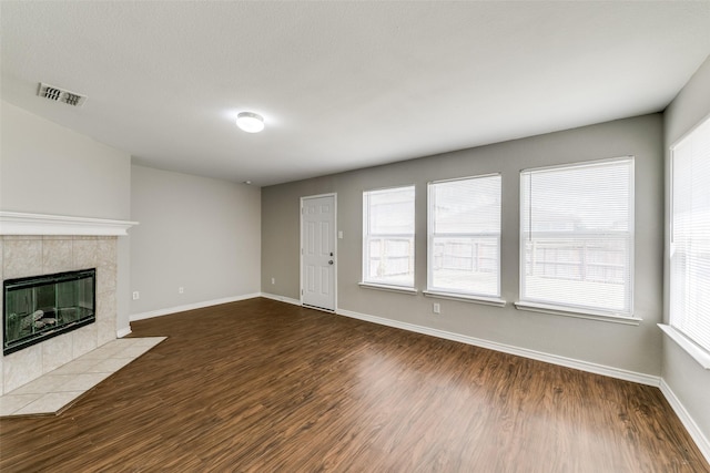 unfurnished living room featuring a tiled fireplace and dark hardwood / wood-style floors