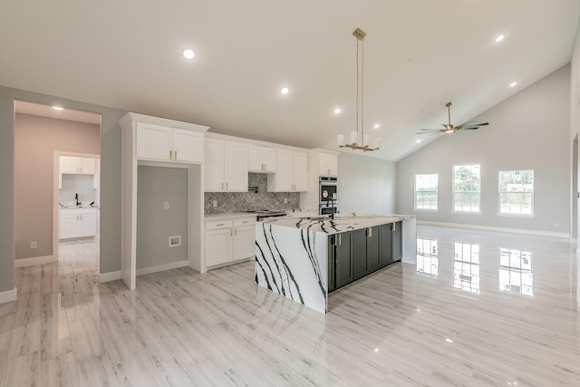 kitchen with white cabinetry, hanging light fixtures, double oven, an island with sink, and decorative backsplash