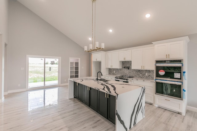 kitchen featuring appliances with stainless steel finishes, decorative light fixtures, an island with sink, sink, and white cabinets