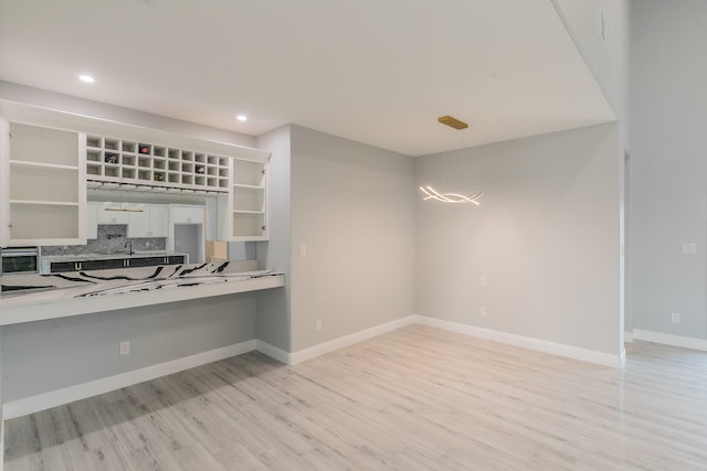 kitchen with pendant lighting, white cabinetry, backsplash, stainless steel oven, and light wood-type flooring