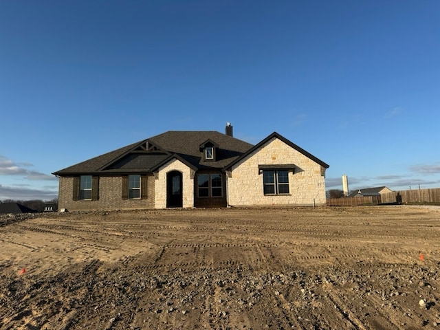 view of front of house featuring stone siding, fence, and a chimney