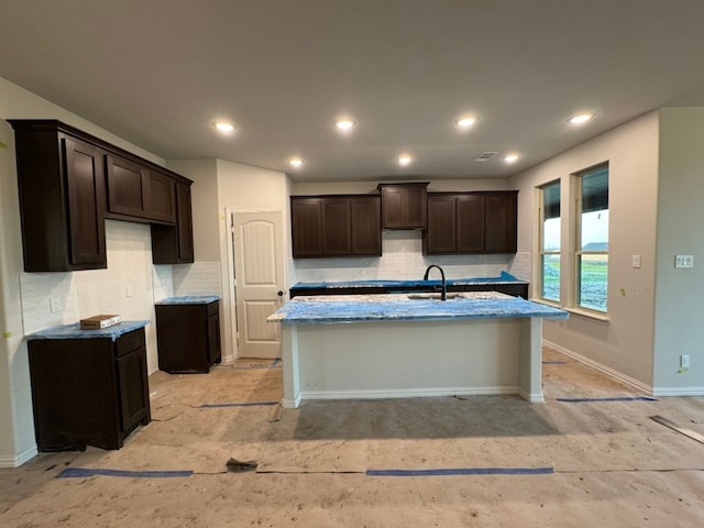 kitchen with tasteful backsplash, a sink, a kitchen island with sink, and recessed lighting