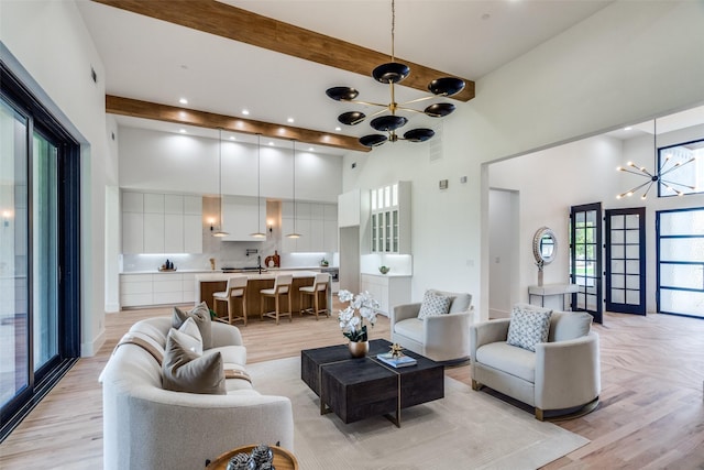 living room featuring an inviting chandelier, a towering ceiling, beam ceiling, and light hardwood / wood-style floors