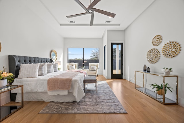 bedroom with ceiling fan, a raised ceiling, light hardwood / wood-style flooring, and access to outside