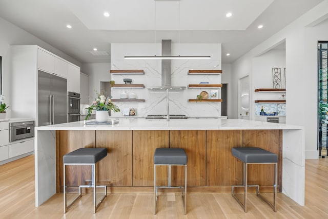 kitchen featuring white cabinetry, wall chimney exhaust hood, a breakfast bar, and a large island with sink