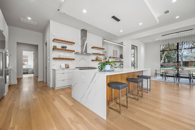 kitchen featuring white cabinets, backsplash, hanging light fixtures, a large island, and wall chimney exhaust hood