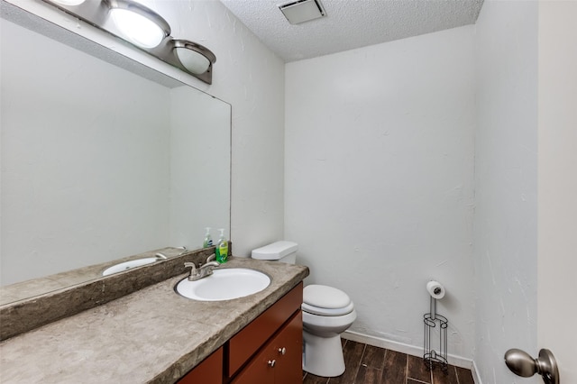 bathroom with hardwood / wood-style flooring, vanity, toilet, and a textured ceiling