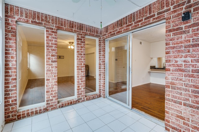 tiled empty room with ceiling fan and brick wall