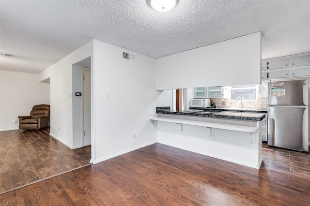 kitchen with stainless steel refrigerator, kitchen peninsula, dark wood-type flooring, and a breakfast bar area