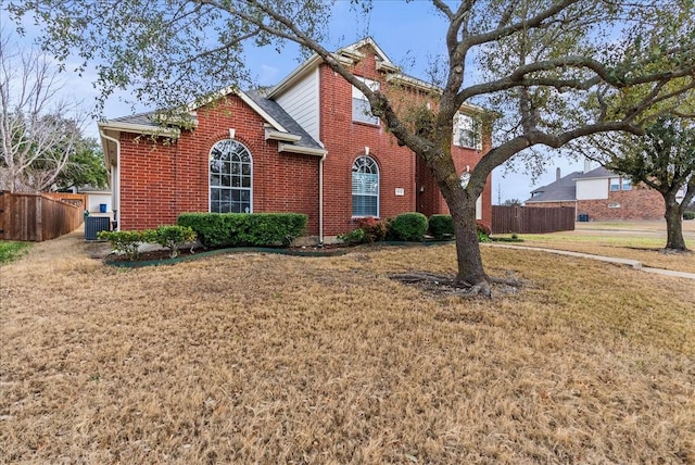 traditional home featuring brick siding, cooling unit, a front lawn, and fence