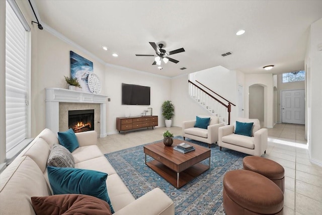 tiled living room with visible vents, stairway, arched walkways, a fireplace, and crown molding