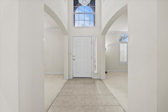 carpeted entrance foyer featuring tile patterned floors, plenty of natural light, baseboards, and ornamental molding