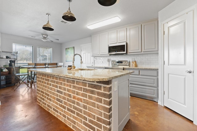 kitchen featuring concrete flooring, tasteful backsplash, decorative light fixtures, appliances with stainless steel finishes, and an island with sink