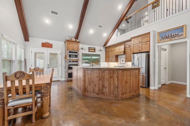 kitchen featuring appliances with stainless steel finishes, french doors, an island with sink, high vaulted ceiling, and light stone countertops