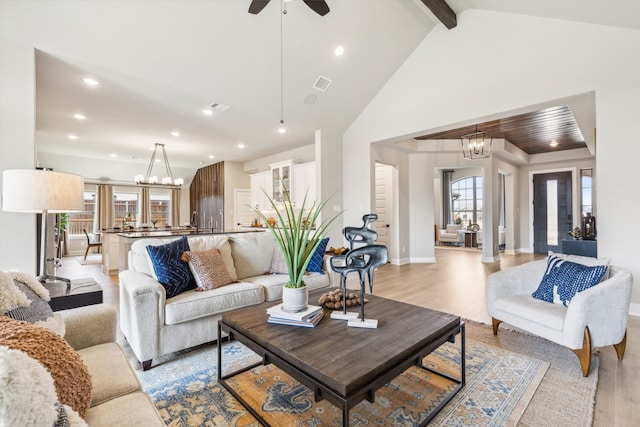 living room with beamed ceiling, high vaulted ceiling, ceiling fan with notable chandelier, and light wood-type flooring