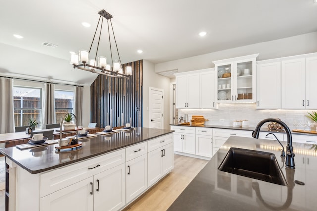 kitchen featuring sink, a kitchen island with sink, hanging light fixtures, white cabinets, and decorative backsplash