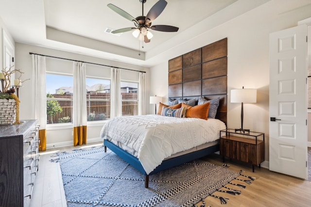 bedroom featuring a raised ceiling, ceiling fan, and light wood-type flooring