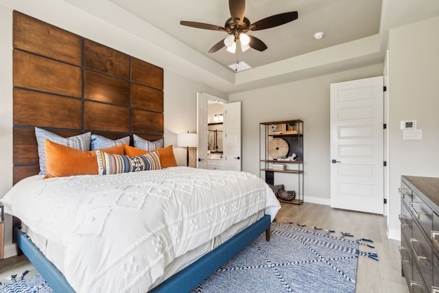 bedroom with light hardwood / wood-style flooring, a raised ceiling, and ceiling fan