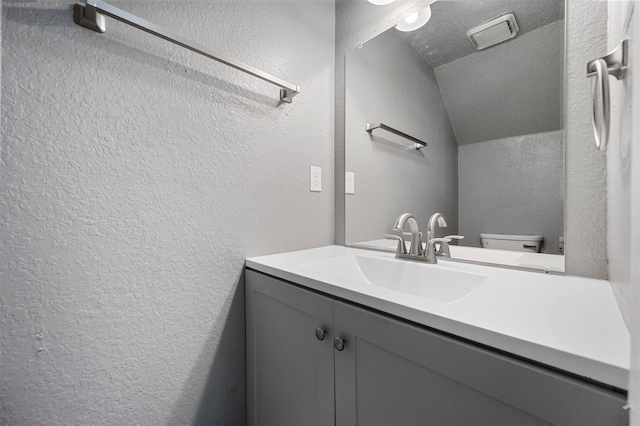 bathroom with lofted ceiling, vanity, a textured ceiling, and toilet