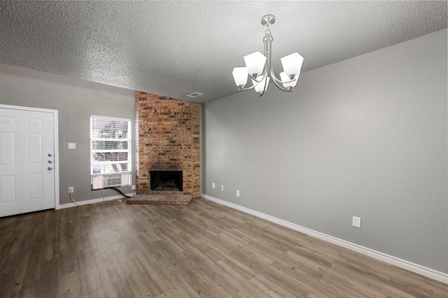 unfurnished living room featuring an inviting chandelier, cooling unit, a brick fireplace, a textured ceiling, and hardwood / wood-style flooring