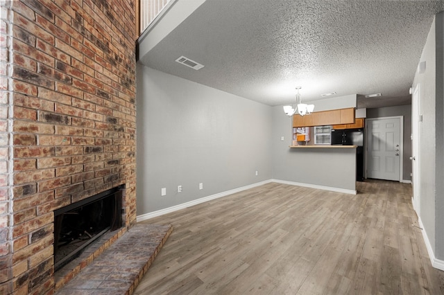 unfurnished living room featuring a textured ceiling, a fireplace, a chandelier, and light wood-type flooring