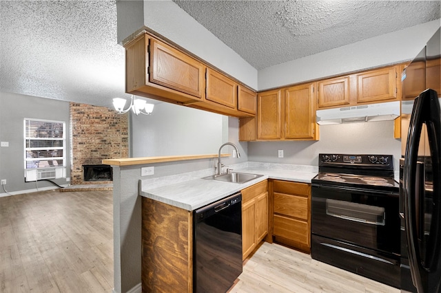 kitchen featuring sink, light hardwood / wood-style flooring, black appliances, a textured ceiling, and a brick fireplace