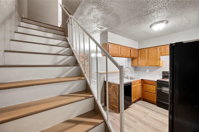 kitchen featuring extractor fan, sink, a textured ceiling, light wood-type flooring, and black appliances