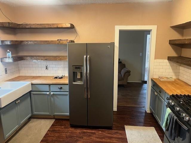 kitchen with butcher block countertops, dark wood-type flooring, stainless steel fridge, backsplash, and range with gas cooktop