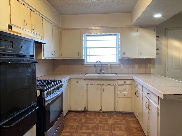 kitchen with sink, gas range, a textured ceiling, dark parquet floors, and oven