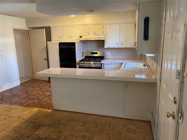 kitchen with sink, white cabinets, tile counters, kitchen peninsula, and gas range