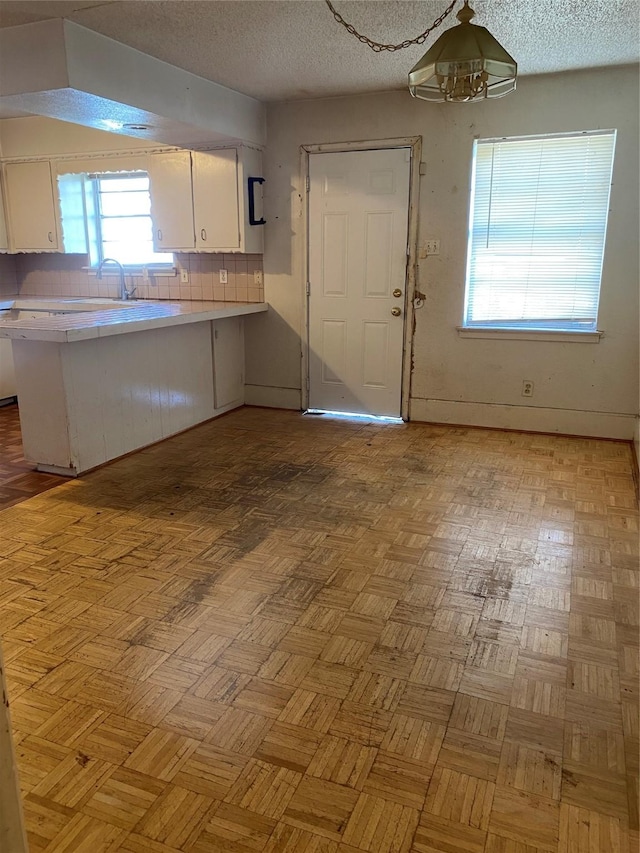 kitchen featuring tasteful backsplash, white cabinetry, light parquet floors, kitchen peninsula, and a textured ceiling