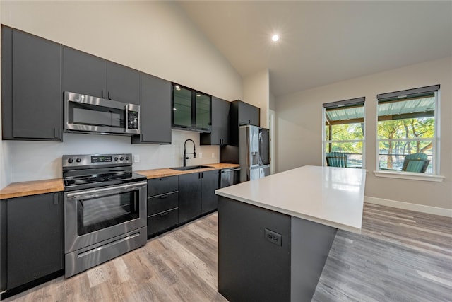 kitchen featuring lofted ceiling, sink, appliances with stainless steel finishes, a kitchen island, and light wood-type flooring