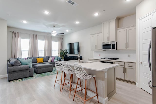 kitchen with sink, a kitchen island with sink, stainless steel appliances, a kitchen breakfast bar, and light hardwood / wood-style floors