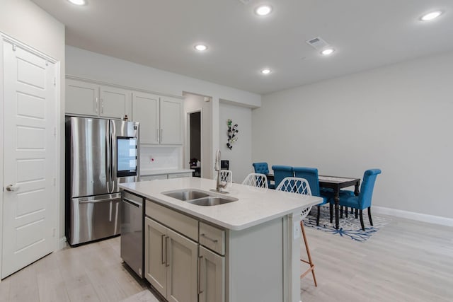 kitchen with a kitchen bar, sink, a center island with sink, light wood-type flooring, and stainless steel appliances