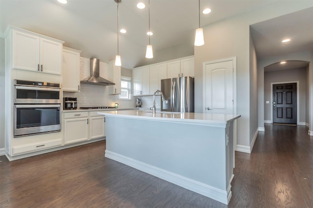 kitchen with white cabinetry, appliances with stainless steel finishes, a center island with sink, and wall chimney exhaust hood