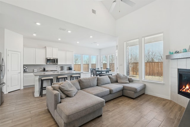 living room with visible vents, high vaulted ceiling, light wood-style flooring, and a tile fireplace