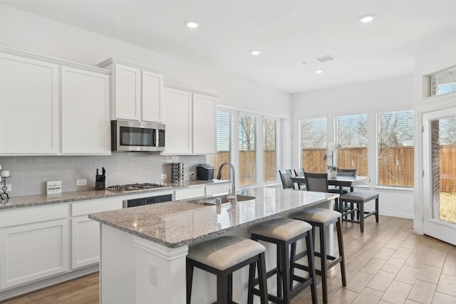 kitchen featuring a kitchen bar, a sink, tasteful backsplash, appliances with stainless steel finishes, and white cabinets