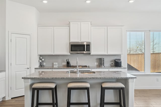 kitchen with stainless steel microwave, backsplash, a breakfast bar, and light wood-style floors