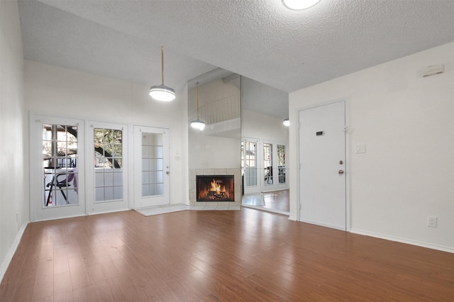 unfurnished living room with a tile fireplace, a textured ceiling, and hardwood / wood-style floors