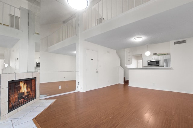 unfurnished living room with light hardwood / wood-style flooring, a towering ceiling, and a tiled fireplace