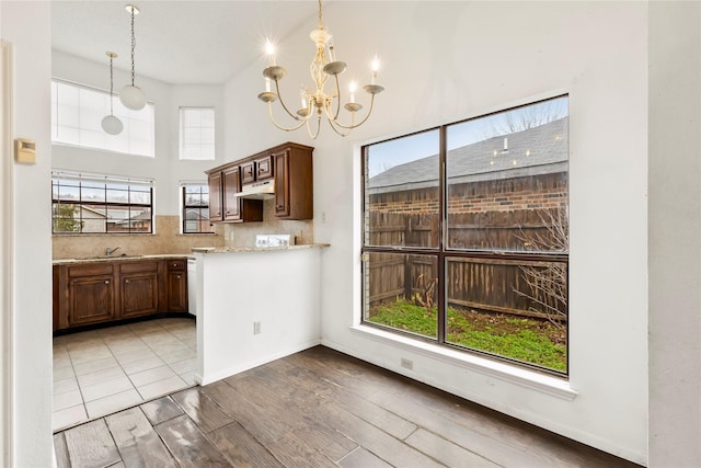 kitchen featuring wood-type flooring, decorative light fixtures, a chandelier, light stone countertops, and backsplash